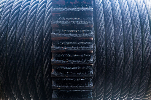 Coiled steel cable, with a large gear in the middle, close-up.