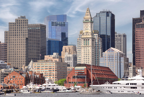Boston skyline with tall buildings, Custom House Tower (a Boston landmark), and waterfront with boats and large yacht anchored in the harbor.