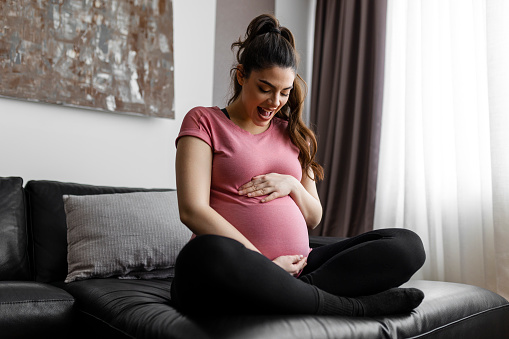 Portrait shot of young beautiful woman on third trimester of pregnancy. Close up of pregnant female with arms on her round belly. Expecting a child concept. Background, copy space.