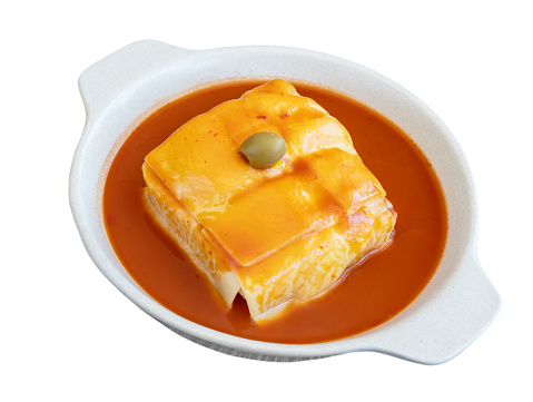 Traditional Portuguese Francesinha with sausage and meat, melted cheese, drizzled with beer sauce and olive. Close-up of the plate on a white background. High quality photo