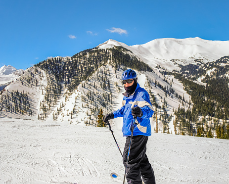 Senior male skier turns and looks at camera; massive mountain range near Aspen, Colorado,  behind him