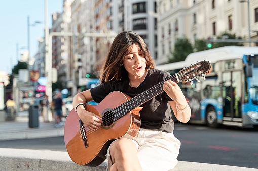 young music student sitting in the city playing the acoustic guitar.