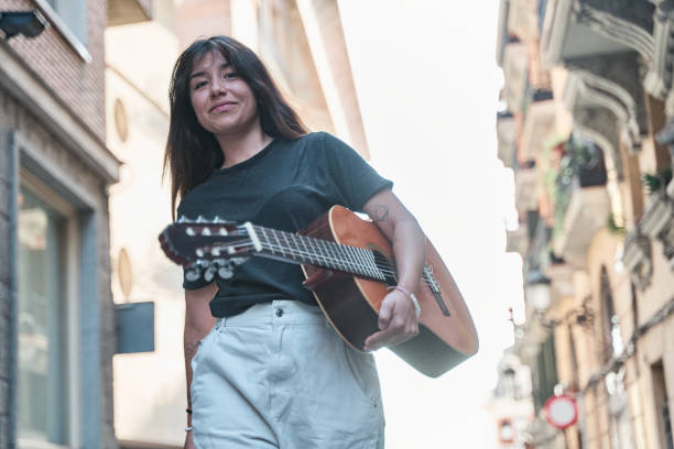 latin woman with afro hair brown skin of average age 25 years from colombia - bogota dressed in light fabric pajamas is on the sofa in her house playing guitar