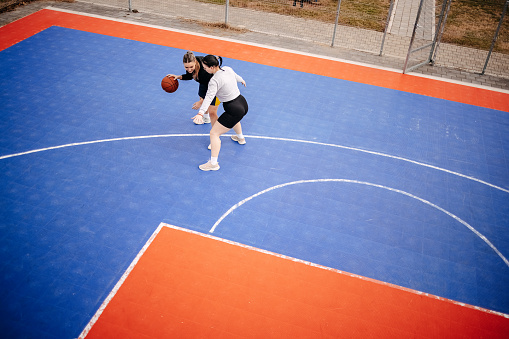 Two women having fun with playing basketball on outdoors court