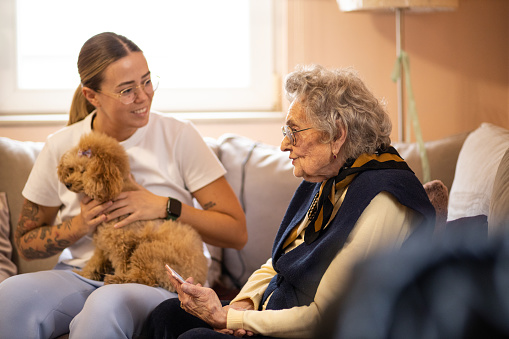 Grandmother and granddaughter talking at nursing home during a visit with her dog. Nurse listening to her elderly patient.