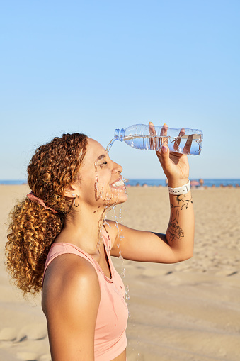 A young girl cools off with cold water during the summer heat. She pours cool water from a bottle to take a break from training. Vertical photo