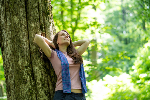 beautiful woman enjoying nature leaning on a tree looking at the sky