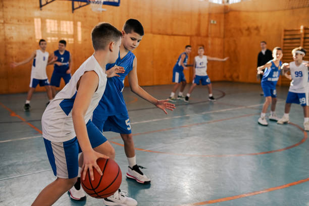 Young athletic boys practicing game at indoor court on training. Junior basketball player is dribbling and guarding a ball while his rival is trying to steal it on training at indoor court. In blurry background are young basketball teammates struggling for a ball. youth basketball indoor stock pictures, royalty-free photos & images