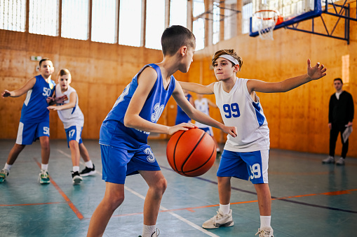 A junior basketball players playing basketball on training and practicing for a match. In foreground are boys in action playing basketball on training. In background are player struggling for a ball.
