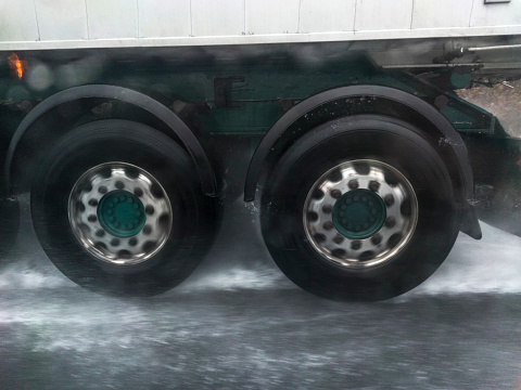 Truck wheels splashing water on road. Dangers driving near trucks