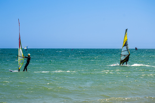 Young girl pulling a sail from the water before windsurfing in a blue ocean in a summertime.