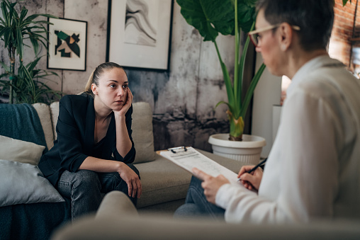 In a serene and inviting space, a therapist attentively listens to their client who is sharing their feelings. The room exudes tranquility with its soft lighting and comfortable furnishings, providing an ideal environment for healing and self-discovery.