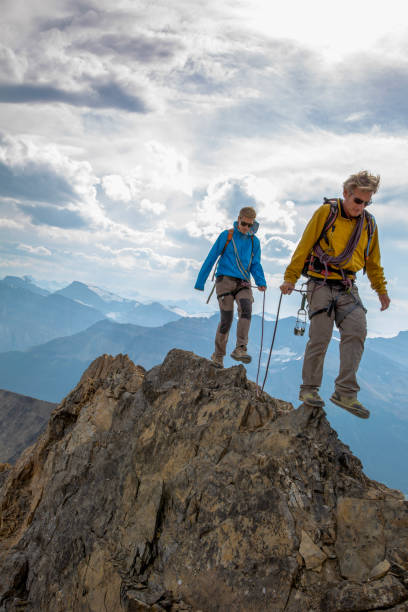 Mountaineers walk along mountain ridge above mountain ranges and below dramatic sky