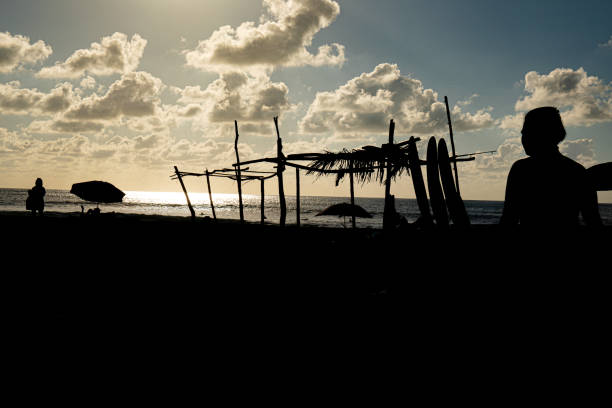 Surfer sitting with surfboard on the beach at sunset.