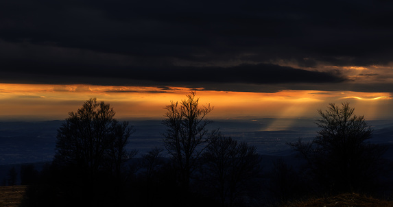 The sun is breaking through heavy, dark storm clouds, casting beams of light across the sky and illuminating the landscape below