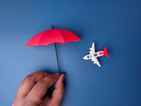 Hand holding red umbrella covered airplane on a blue background