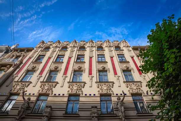 Picture of a typical art nouveau facade of Riga, Latvia. The Riga Art Nouveau district, located in the Latvian capital, is notable for its concentration of early 20th-century architecture. This area represents one of the highest densities of Art Nouveau architecture globally, distinguished by its elaborate decorative elements and innovative designs that marked a departure from the architectural norms of the period. Art Nouveau in Riga is characterized by its use of asymmetry, geometric shapes, and natural motifs, as well as its incorporation of then-modern materials and building techniques. The façades of the buildings in this district often feature intricate stonework, sculptural reliefs, and wrought-iron details. The district's significance lies not only in its architectural beauty but also in its representation of a particular historical moment of cultural and economic development in Riga. This architectural style flourished during a time of significant growth for the city, coinciding with a broader European movement that sought to break away from the historical revival styles of the 19th century. While the area is a popular tourist destination, it also remains a functional part of the city, with many of the buildings still serving as residences and businesses. The Riga Art Nouveau Museum, which is situated within the district, serves as an educational institution, providing insights into the Art Nouveau movement and its manifestation in Riga.
