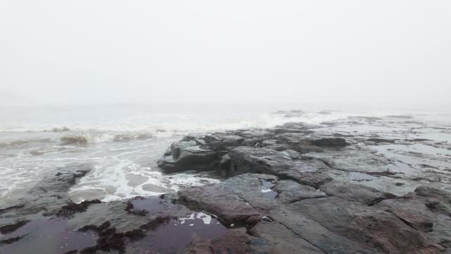 Very mist and foggy scene on the coast of the UK. Winters coastal seascape with small boats and rough seas crashing against the rocks and cliffs on the east coast of the UK. English cold spell