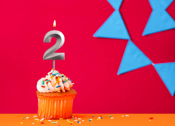 istock Number 2 candle with birthday cupcake on a red background with blue pennants 2041655579
