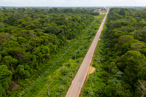 Aerial drone view of a paved highway cutting through the Amazon rainforest with a small town nestled in the verdant backdrop.