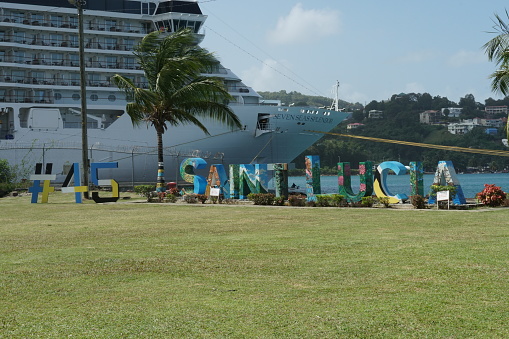 Titel: Castries, St Lucia 02.02.2024: Large coloured letters with the word Saint Lucia and number 45 exhibited in small park in front of passenger terminal with huge cruise vessel Seven Seas Splendor.