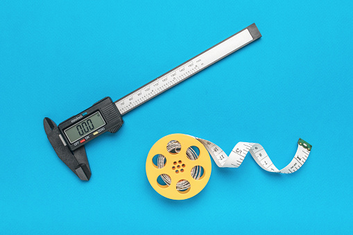 A coil with a measuring tape and a caliper on a blue background. A tool for accurate measurement of dimensions.