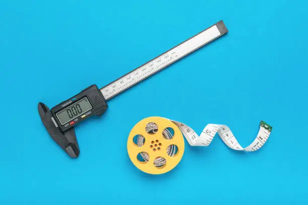 A coil with a measuring tape and a caliper on a blue background. A tool for accurate measurement of dimensions.