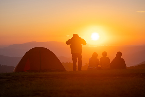 Group of friend sitting by the tent during overnight camping while looking at the beautiful view point sunset over the mountain for outdoor adventure vacation travel concept