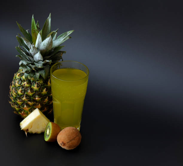 a tall glass glass of fruit juice on a black background, next to a ripe pineapple and kiwi slices. - healthy eating food and drink nutrition label food imagens e fotografias de stock