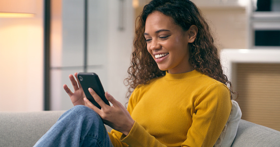 Home, smile and woman with a smartphone, typing and connection with social media, relax or contact. Person, post or girl on a sofa, cellphone or network to search internet, mobile user or digital app