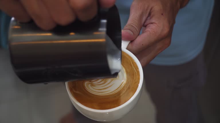 Barista pouring milk to make coffee latte art. b-roll footage video 4k. Cafe business shop. Professional man making pouring steamed milk with espresso to make latte art coffee. Cappuccino.