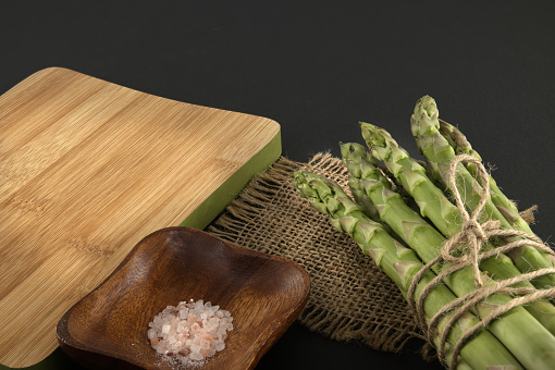 Bunch of green asparagus tied with jute cord near cutting board over a black background with copy space. Asparagus cooking and spring vegetable concept