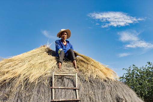 village african woman repairing a thatched roof, manual labor in a sunny day outdoors