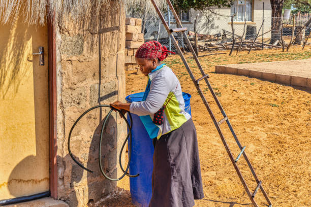 anciana africana de aldea con una pipa llenando los bidones de agua al lado de su casa, para mejorar la vida en las zonas rurales - african descent drum african culture day fotografías e imágenes de stock