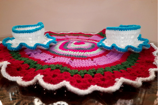 View of woollen, knitted craftwork consisting of circular mat, cups and saucers