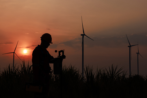 Silhouette of young men engineer standing checking equipment wind turbine beside agricultural sugarcane and wind turbine morning sunlight background,