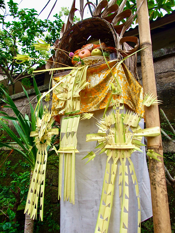 Closeup photo of a beautiful multicoloured decoration of folded and cut coconut palm leaves, marigold flowers, fruit offerings, coloured paper, vibrant cloth and bamboo poles built in front of a Balinese family compound as an offering to the spirits of deceased family on their return to the home during Galungan Festival.