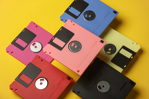 Floating colored retro 80s floppy disks on a yellow background. Conceptual pop, creative layout