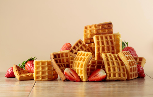 Belgian waffles with strawberries on a beige ceramic table.