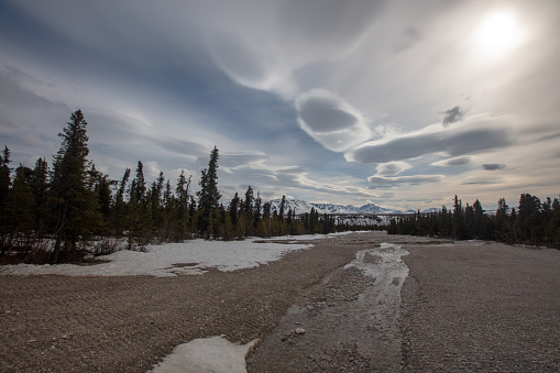 Gravel riverbed and snowcapped mountains under lenticular clouds in the spring in Denali National Park in Alaska United States