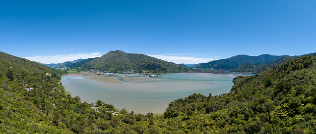 Enjoy the breathtaking panoramic view of Havelock city in New Zealand, with a tranquil lake and rainforest in the foreground. Explore this picturesque urban landscape.
