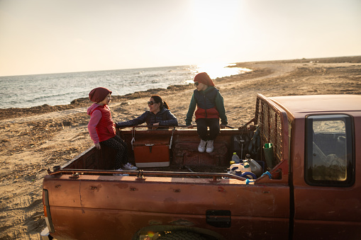 High angle shot of mother and her two children having fun while playing with pebbles in their pick-up truck on the beach at sunset