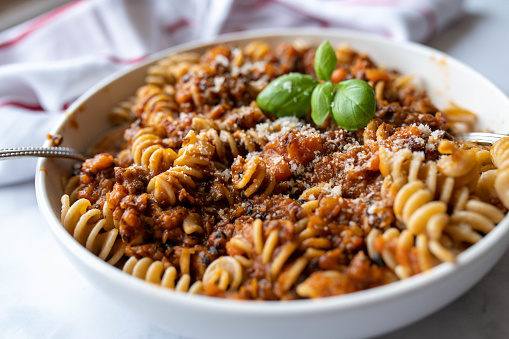 Delicious vegan meal with homemade lentil bolognese and fusilli pasta. Served ready to eat on a deep plate with basil leaf on kitchen table background. Closeup