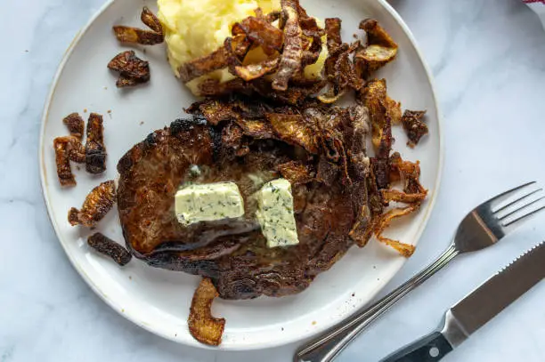 Beef Steak or ribe eye with fried onions and mashed potatoes on a plate isolated on light kitchen background. Close up