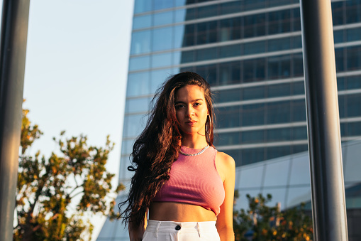 Portrait of a young brazilian woman looking at the camera standing outdoors in the city wearing summer clothes