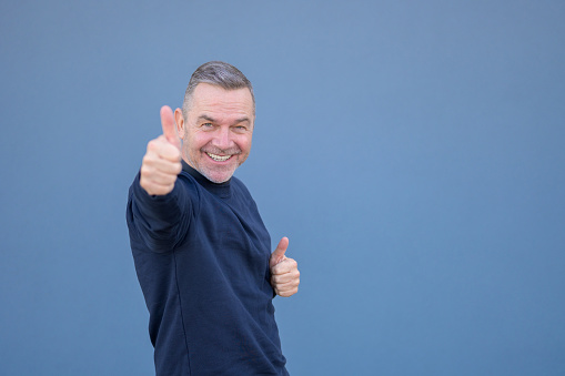 Enthusiastic motivated attractive middle aged man giving a thumbs up gesture of approval and success with a beaming smile