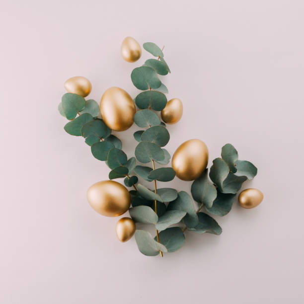 istock Golden eggs with green eucalyptus leaves. Easter decoration pastel pink background. Top view square 2042147510