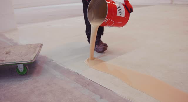 Worker coating floor with epoxy resin in an industrial hall.