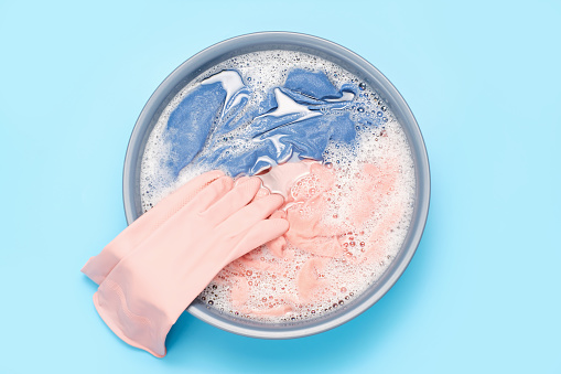 Colorful clothes washed with a basin with soap bubbles close up on a blue background, top view.