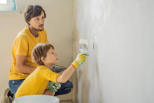 man with his son makes repairs at home, he teaches children to plaster the walls with a spatula in his hands - plaster plasterer work tool child foto e immagini stock